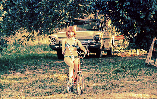 Vintage image form the seventies of a woman riding on bike in a summer day at the countryside.