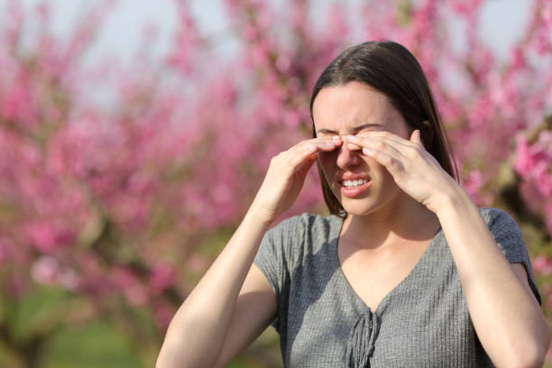 Woman scratching itchy eyes in spring in a flowers field stock photo
