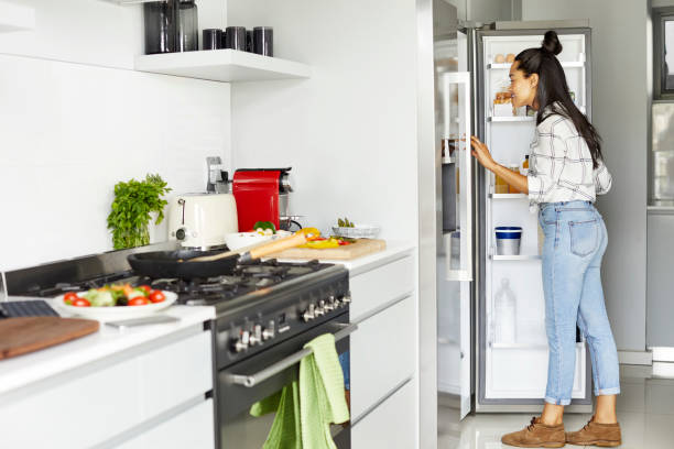 vrouw die voedsel in koelkast bij keuken zoekt - fridge stockfoto's en -beelden