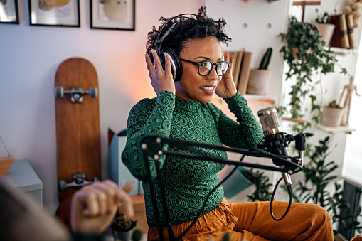 Young women adjusting and wearing headphones with eyeglasses while recording podcast using microphone in studio