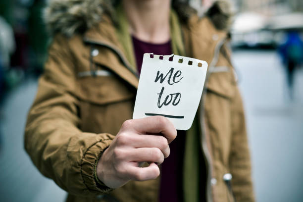woman showing a note with the text me too closeup of a young caucasian woman in the street showing a piece of paper with the text me too written in it me too social movement stock pictures, royalty-free photos & images
