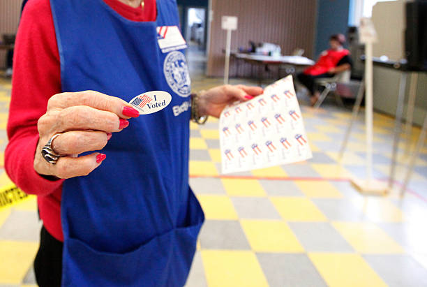Woman showing the I voted sticker Volunteer handing out I Voted stickers after filling out a election ballot at a district voting station polling place stock pictures, royalty-free photos & images