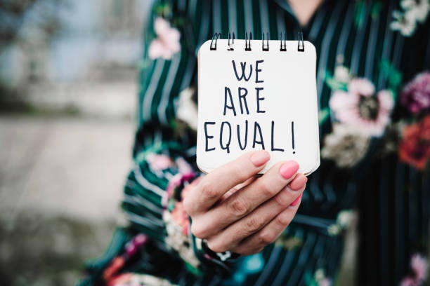 woman shows notepad with the text we are equal closeup of a young woman outdoors showing a notepad in front of her with the text we are equal written in it women's rights stock pictures, royalty-free photos & images