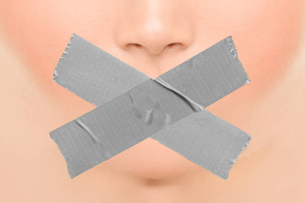 Woman silenced with adhesive duct tape covering closed mouth. Censorship, shut down of freedom of speech. Face nose and lips. Woman silenced with adhesive duct tape covering closed mouth. Censorship, shut down of freedom of speech. Face nose and lips. human mouth gag adhesive tape women stock pictures, royalty-free photos & images