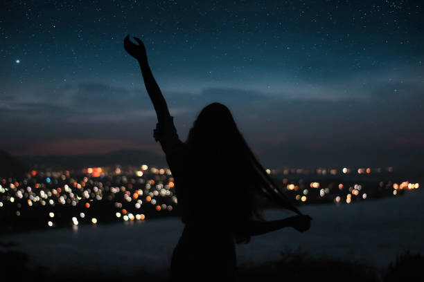 Photo of woman silhouete touching the stars long hair with night city on the background