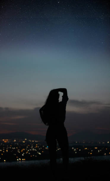 Photo of woman silhouette back gazing the stars with city on the background