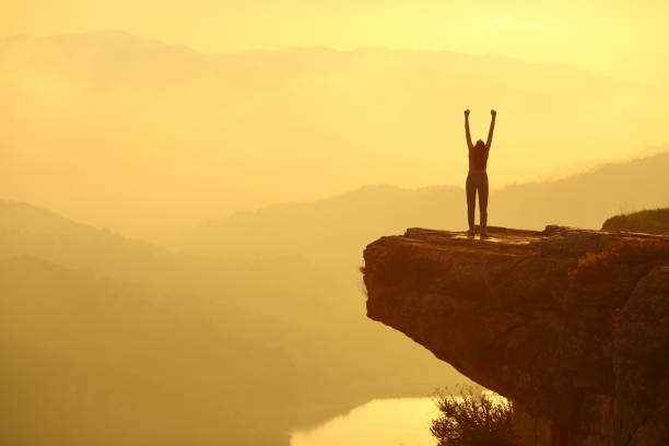 Woman silhouette celebrating in the top of a cliff stock photo