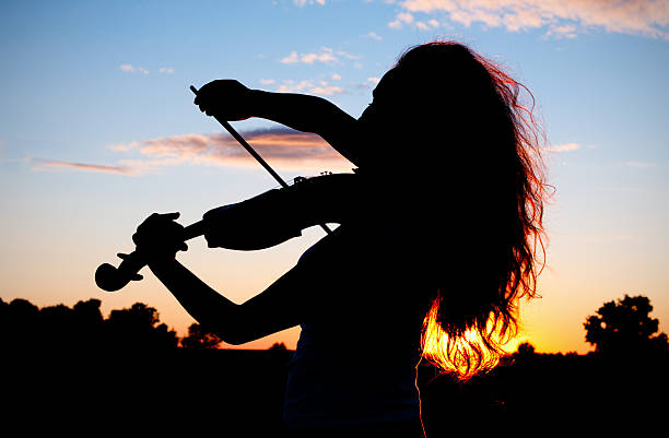 Woman silhouette playing violin in sunset light stock photo