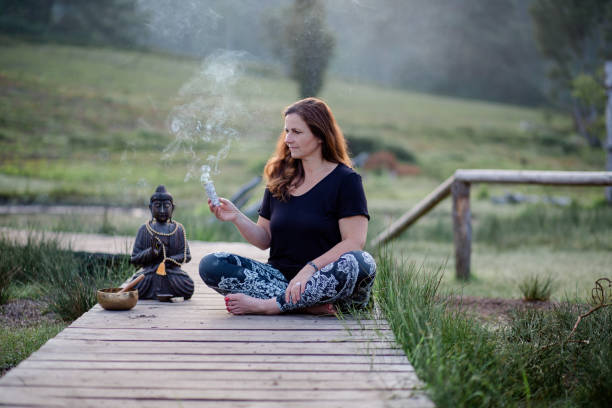 Woman sits on a boardwalk and holds a lighted bundle of sage in her hand Woman with dark hair holds a bundle of sage in her hand for a spiritual ritual sage stock pictures, royalty-free photos & images