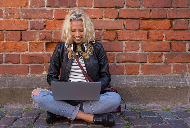 woman sitting by the brick wall and working on laptop - hogeschool rood samen stockfoto's en -beelden