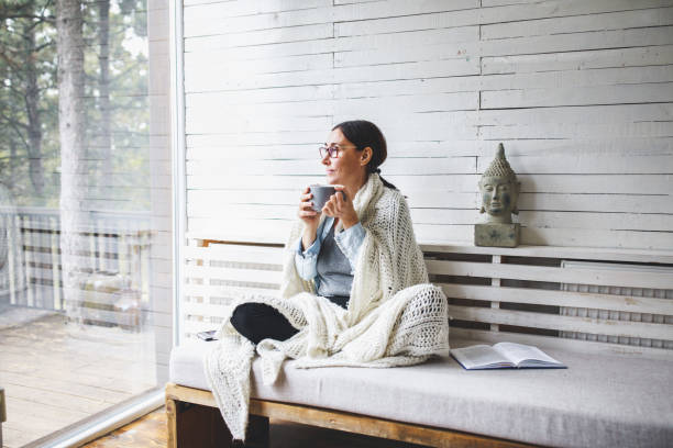 vrouw zit comfortabel en kijkt door het raam - woman drinking coffee stockfoto's en -beelden