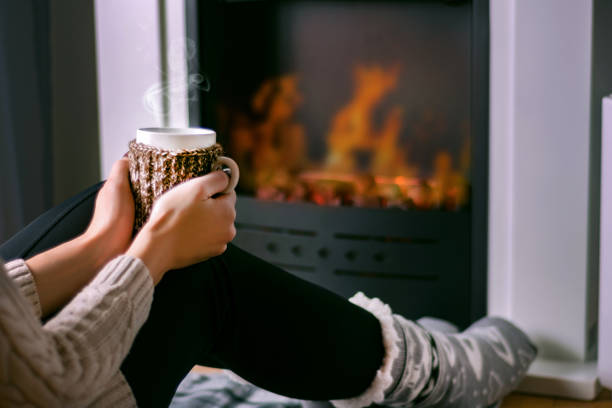 Woman sitting in front of the fireplace and holding cup of tea in hand on legs stock photo