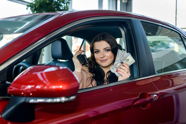 Woman sitting in new car and showing dollars and keys stock photo