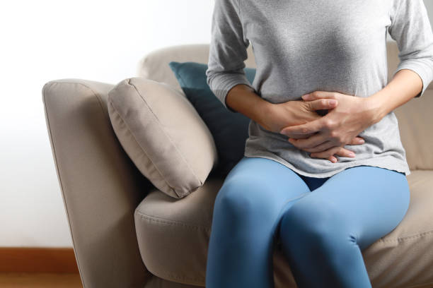 ソファに座ってお腹を抱いている女性。胃痛の概念 ストックフォト