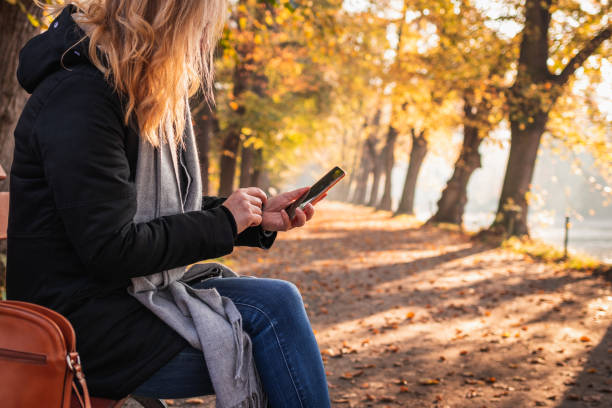 Woman sitting on bench in autumn park and using smart phone stock photo