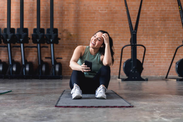 Woman sitting on exercise mat laughs with unseen person stock photo