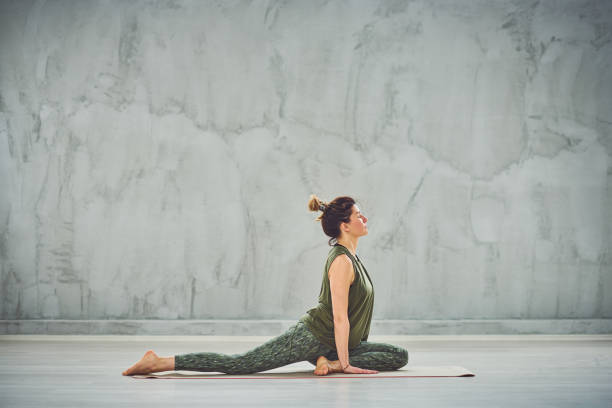 Woman sitting on mat in pigeon yoga pose. stock photo