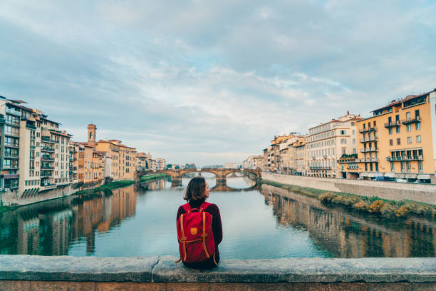 Woman sitting on Ponte Veccio and looking at view Young Caucasian woman sitting on Ponte Veccio in Florence  and looking at view, Italy arno river stock pictures, royalty-free photos & images