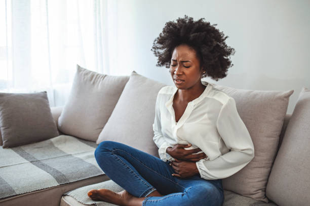 Woman Sitting On Sofa Suffering From Stomach Pain. Woman Sitting On Sofa Suffering From Stomach Pain. Unhealthy young woman with stomachache leaning on the couch at home. Woman lying on her sofa alone and suffering from period cramps at home endometriosis photos stock pictures, royalty-free photos & images