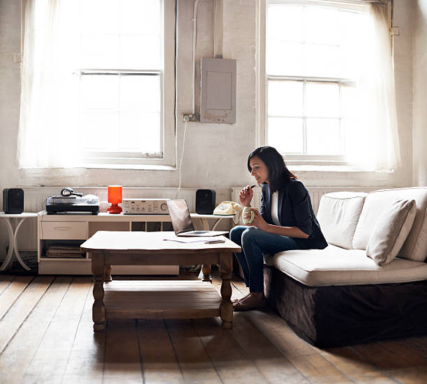 woman sitting on sofa using laptop - windows laptop table stockfoto's en -beelden