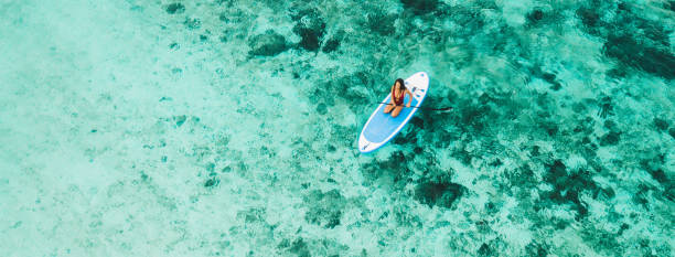 Woman sitting on sup board and enjoying turquoise transparent water and coral reef. Tropical travel, wanderlust and water activity concept. stock photo