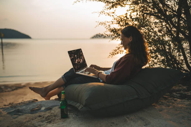 Woman sitting with laptop on the summer beach Woman sitting with laptop on the summer beach at sunset nomadic people stock pictures, royalty-free photos & images