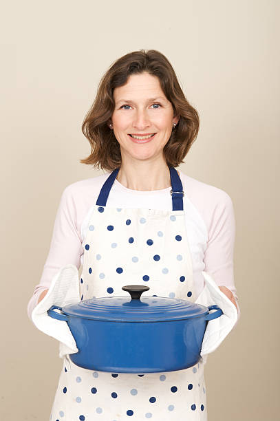 Woman smiling because she knows how easy crock pots are. Smiling woman with large blue cooking pot casserole dish stock pictures, royalty-free photos & images