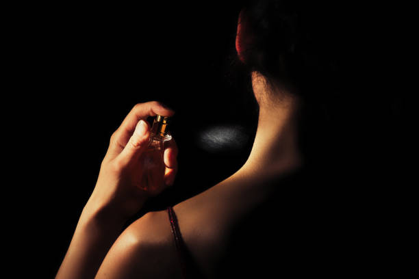Woman sprays perfume on her neck with a black background stock photo