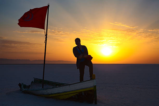 Woman standing on boat agaist sunrise Woman silhouette with flag of Tunisia against sunrise lights. Broken boat on salina area tunisia woman stock pictures, royalty-free photos & images