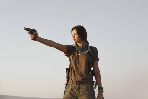 Woman Standing With a Gun Outdoors in Desert Woman standing holding a gun and rope outdoors in the desert. Young brutal dangerous girl with a weapon in confident pose. War action movie style beautiful armed female soldier dressed in stylish military clothes. Special forces serious woman aiming, ready for the attack. actress stock pictures, royalty-free photos & images