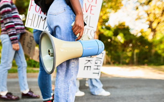 Close-up of a young woman with a megaphone standing with a diverse group of protestors holding signs during a women's rights day march