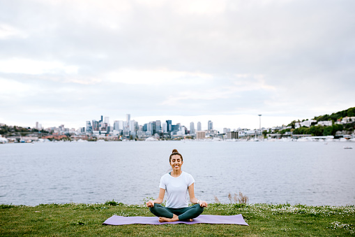 An adult woman takes time for self care in an urban park setting of Seattle, Washington.  The city is visible over Lake Union in the background.