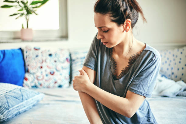 Woman suffering from elbow pain while sitting on bed. stock photo