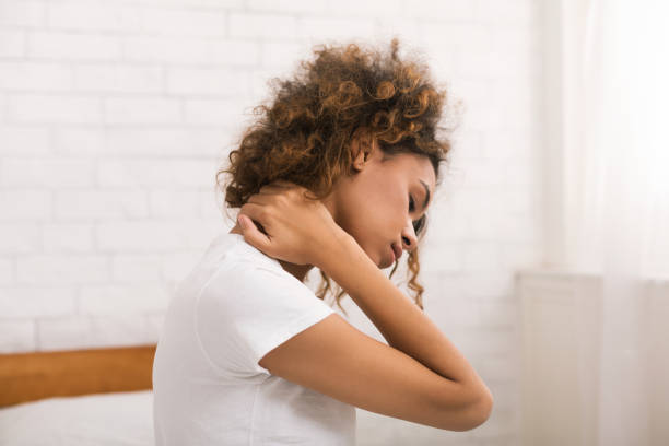 Woman suffering from neck pain, waking up in the morning Woman suffering from neck pain, waking up in the morning, sitting on bed cramp stock pictures, royalty-free photos & images