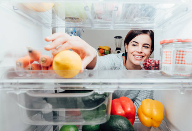 vrouw die een citroen uit de koelkast neemt - fridge stockfoto's en -beelden