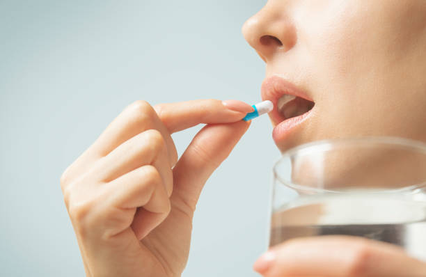 Woman taking a medication capsule or vitamin with glass of water. stock photo