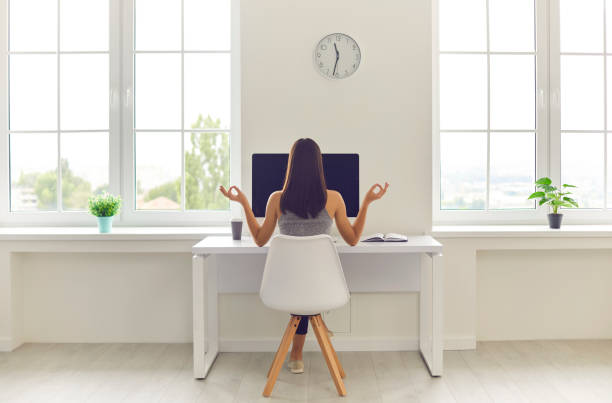 Woman taking break from work and meditating sitting at office table with computer and coffee stock photo