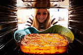 Woman Taking Cooked Dish Of Lasagne Out Of The Oven. Smiling