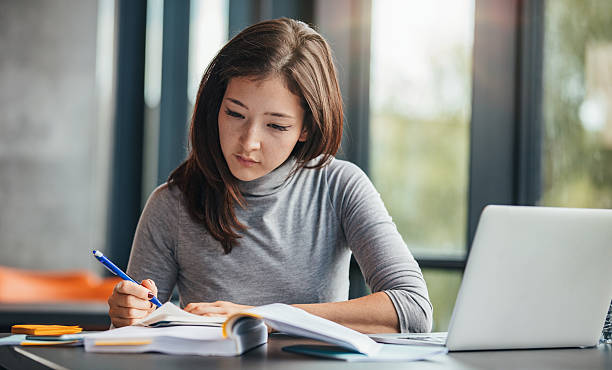 Woman taking down notes in diary Shot of young woman taking down notes in diary. Female university student preparing note for the exam at library. textbook stock pictures, royalty-free photos & images