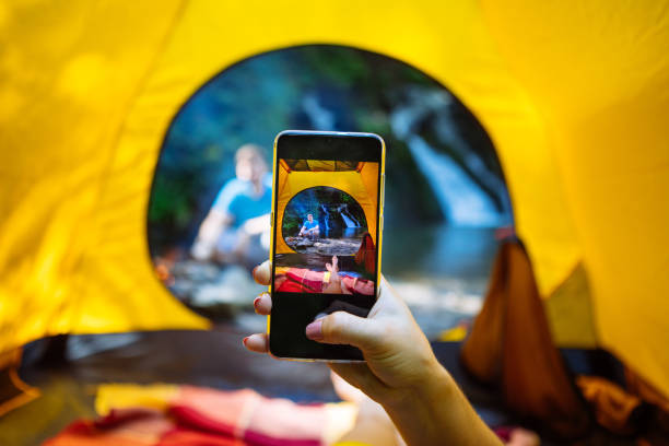woman taking picture on phone from the tent of man near bonfire stock photo