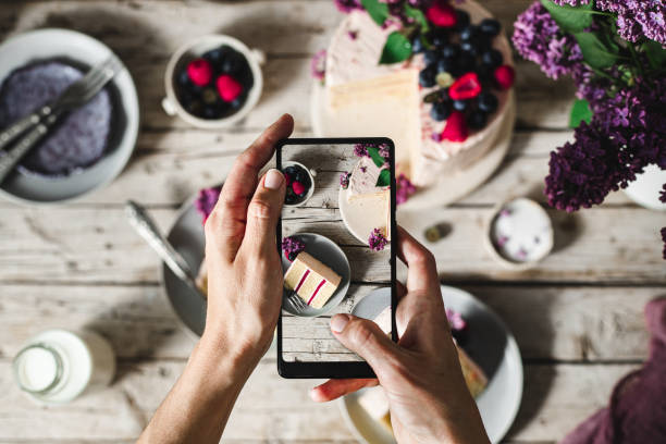 Woman taking pictures of a fruit and flower cake with her hone POV shot of a female chef hands taking photograph of a freshly make cake with her mobile phone. Woman taking pictures of a fruit and flower cake served on table. spread food photos stock pictures, royalty-free photos & images