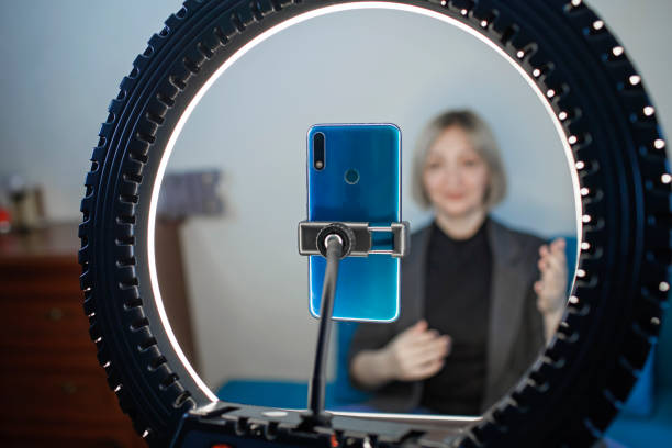 Woman talking to camera and recording video with smartphone and ring light lamp at home, vlogger stock photo