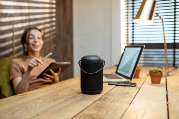 Woman talking to the smart speaker indoors Woman talking to the smart speaker while working on the digital tablet at cozy home office. Concept of a smart home and Artificial Intelligence speech recognition stock pictures, royalty-free photos & images