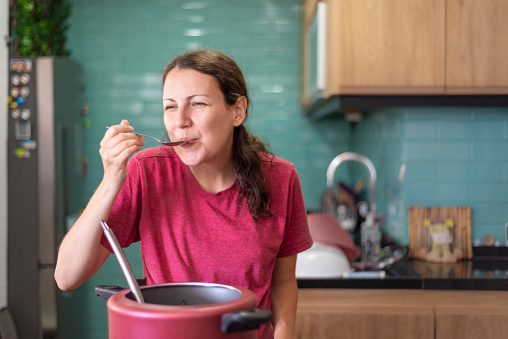 Woman smiling while tasting the food she cooked with a spoon