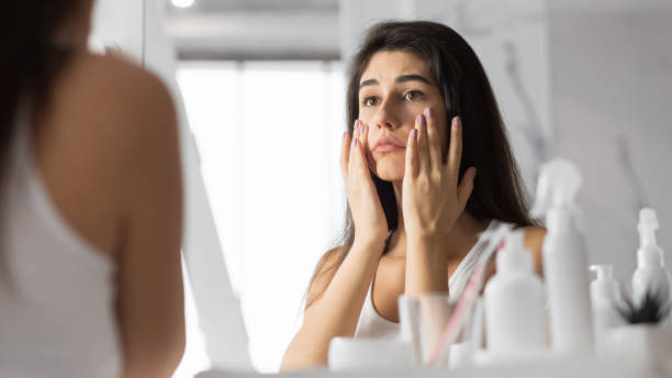 Woman Touching Face Looking At Skin In Mirror At Bathroom Anti-Wrinkle Skincare. Sad Young Woman Touching Face Looking At Her Skin In Mirror At Bathroom. Selective Focus, Panorama tired stock pictures, royalty-free photos & images