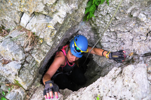 Woman tourist exiting a cave through very narrow opening, wearing via ferrata gear. Location: Dragons Amphitheater (Amfiteatrul Zmeilor) route in Baia de Fier, Gorj county, Romania. stock photo