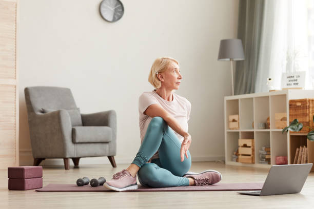Woman training at home Senior woman sitting on the floor on exercise mat in front of laptop and training at home relaxation exercise stock pictures, royalty-free photos & images