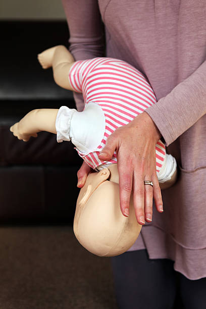 A woman trains to help a baby that is choking Woman showing on a dummy what to do when a baby is choking. choking photos stock pictures, royalty-free photos & images