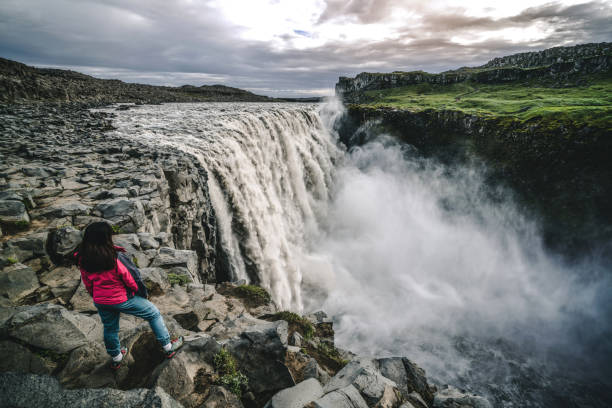 Woman traveler at amazing Iceland landscape of Dettifoss waterfall in Northeast Iceland. Dettifoss is a waterfall in Vatnajokull National Park reputed to be the most powerful waterfall in Europe. Woman traveler at amazing Iceland landscape of Dettifoss waterfall in Northeast Iceland. Dettifoss is a waterfall in Vatnajokull National Park reputed to be the most powerful waterfall in Europe. iceland dettifoss stock pictures, royalty-free photos & images