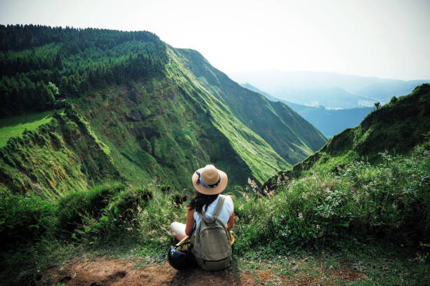 woman traveler in azores woman traveler holding hat and looking at amazing mountains and forest, wanderlust travel concept, space for text, atmospheric epic moment, azores ,portuhal, ponta delgada, sao miguel acores stock pictures, royalty-free photos & images